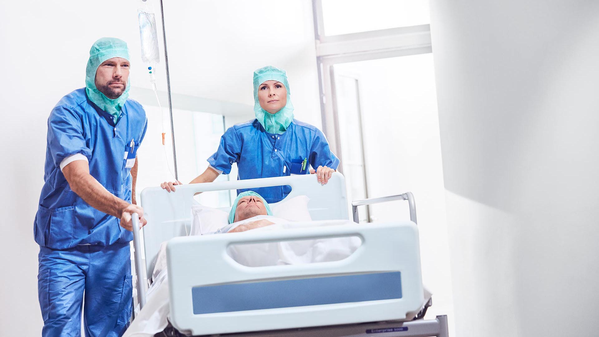 Helsepersonell som triller en pasient i sykehusseng